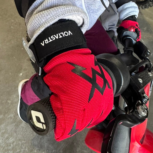 Kid wearing a red and black Voltastra OG Glove with a logo on a dirt bike.