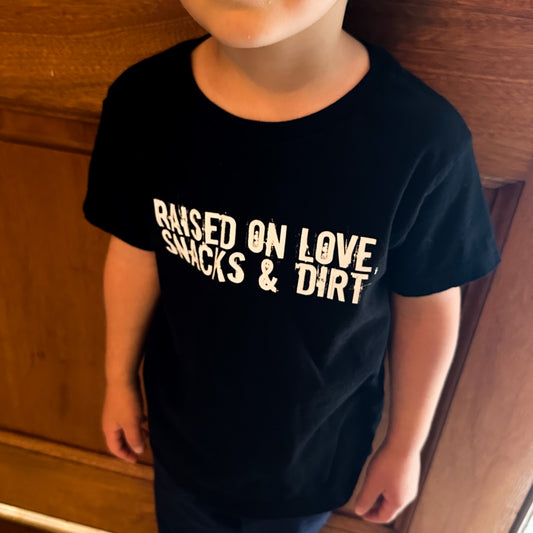 Child wearing a black t-shirt with the words "Raised on Love, Snacks & Dirt" across the front