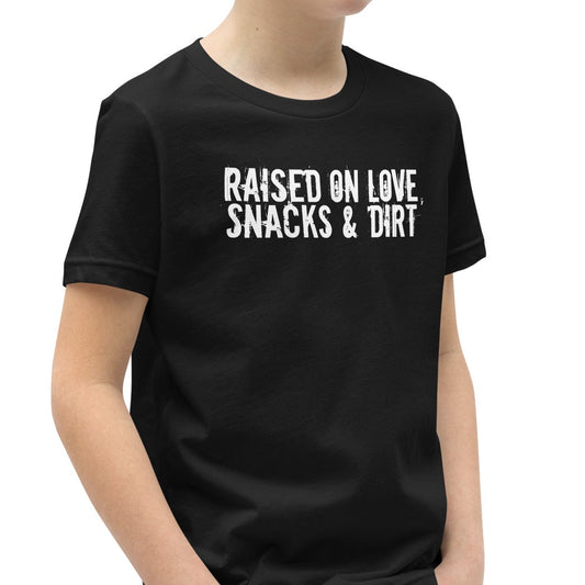 Child wearing a black t-shirt with white text 'Raised on Love, Snacks & Dirt' in a grungy font
